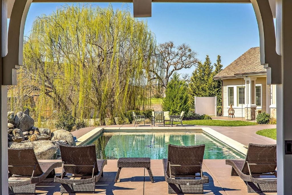 Frontier Farmhouse - Exterior - View from portella towards lounge chairs and pool with willow tree and six person seating area in the distance